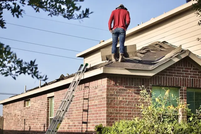 Man wearing a red hoodie standing on the roof and fixing it