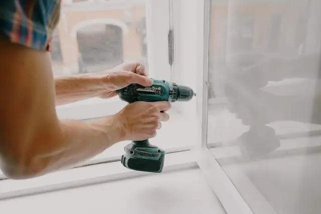 a man drilling into a white window frame